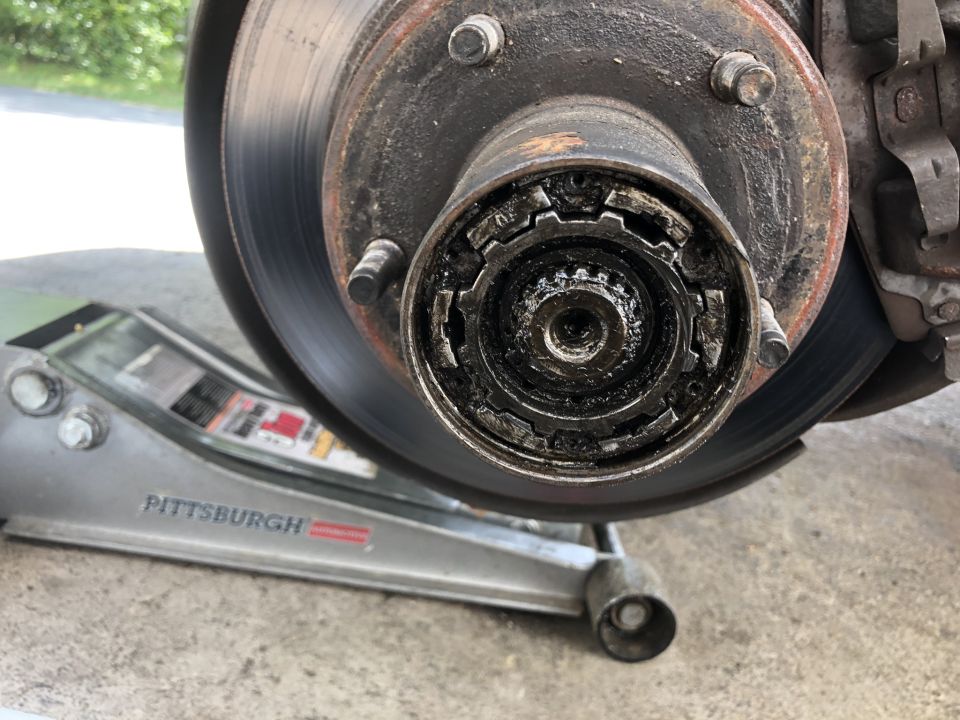 Vehicle wheel hub with manual locking hub mechanism and grease, supported by a floor jack.