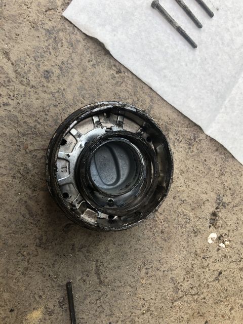 1995 Ford Bronco - A close-up overhead view of a dirty, metallic automotive part, possibly a hub or bearing assembly, resting on a concrete surface next to a…