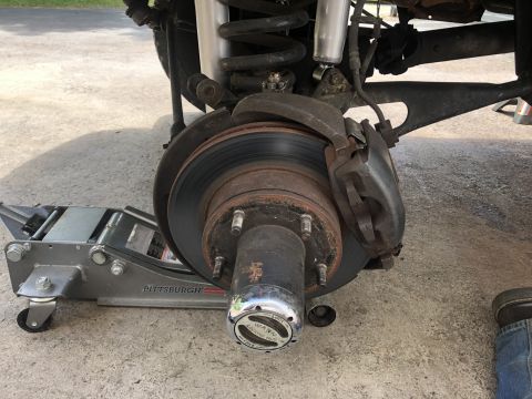 1995 Ford Bronco - A close-up view of the front driver's side brake rotor, caliper, and hub assembly of a vehicle supported by a Pittsburgh Automotive floor j…