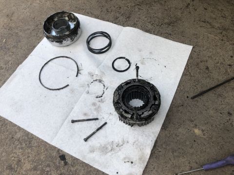 1995 Ford Bronco - Disassembled transmission parts are laid out on a white paper towel on a concrete surface. Visible parts include a metal housing with a spr…