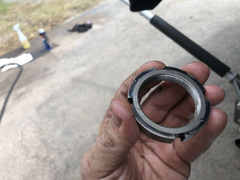 1995 Ford Bronco - A hand holds a threaded locknut with four notches around its outer edge. The locknut appears to be made of metal and has visible wear and g…