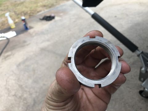 1995 Ford Bronco - A hand holds a threaded locknut with notches around its circumference. In the background, a portion of a vehicle jack and some cleaning sup…