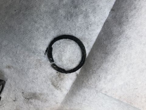 1995 Ford Bronco - A close-up view shows a broken black metal ring with two holes on its inner circumference, resting on a white textured surface.
