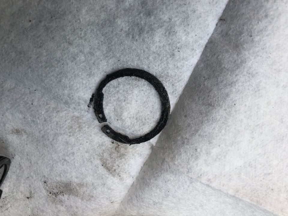 Broken black metal ring with two holes on white textured surface