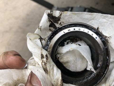 1995 Ford Bronco - A close-up of a dirty bearing with the stamped text "LM 501349" is being held by a hand and wiped with a paper towel.