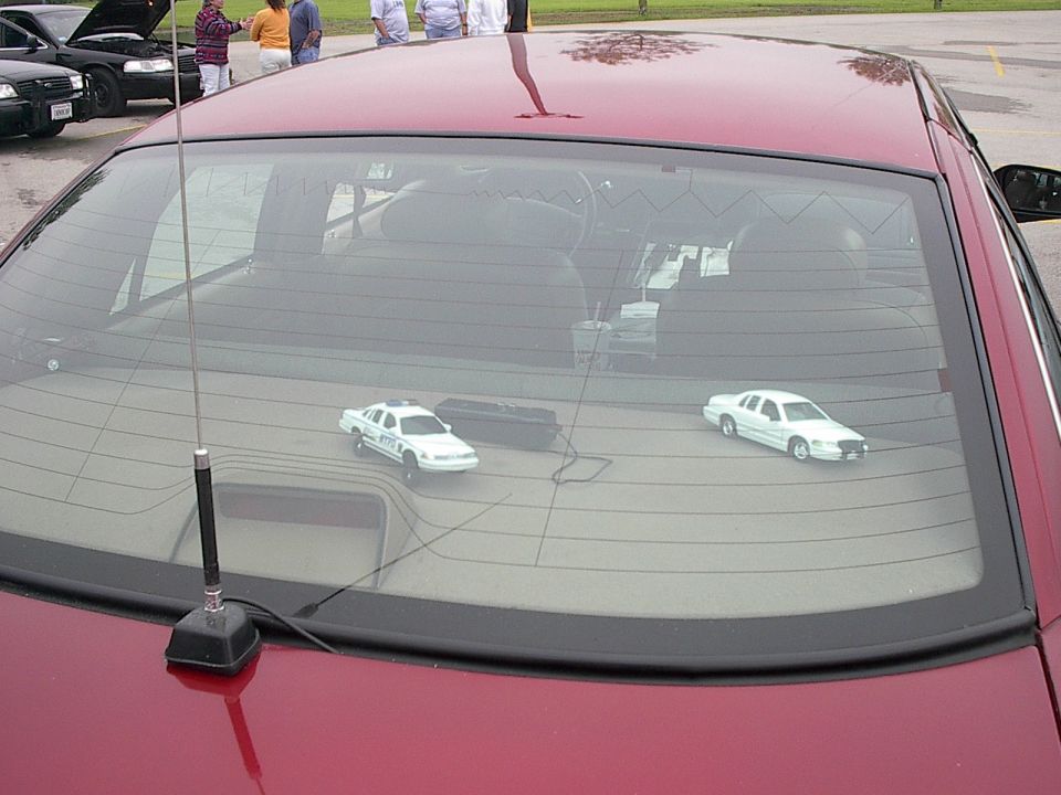 Rear window of a red sedan with two toy cars inside: a white police car and a white sedan.