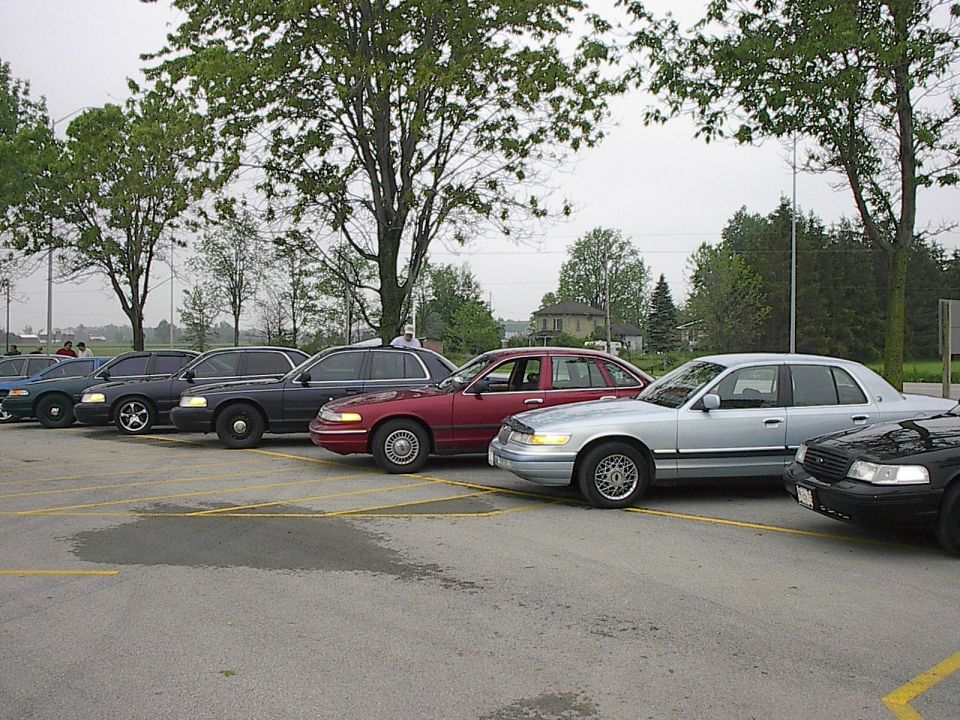 Silver Mercury Grand Marquis and red sedan parked in a lot with trees and a building.