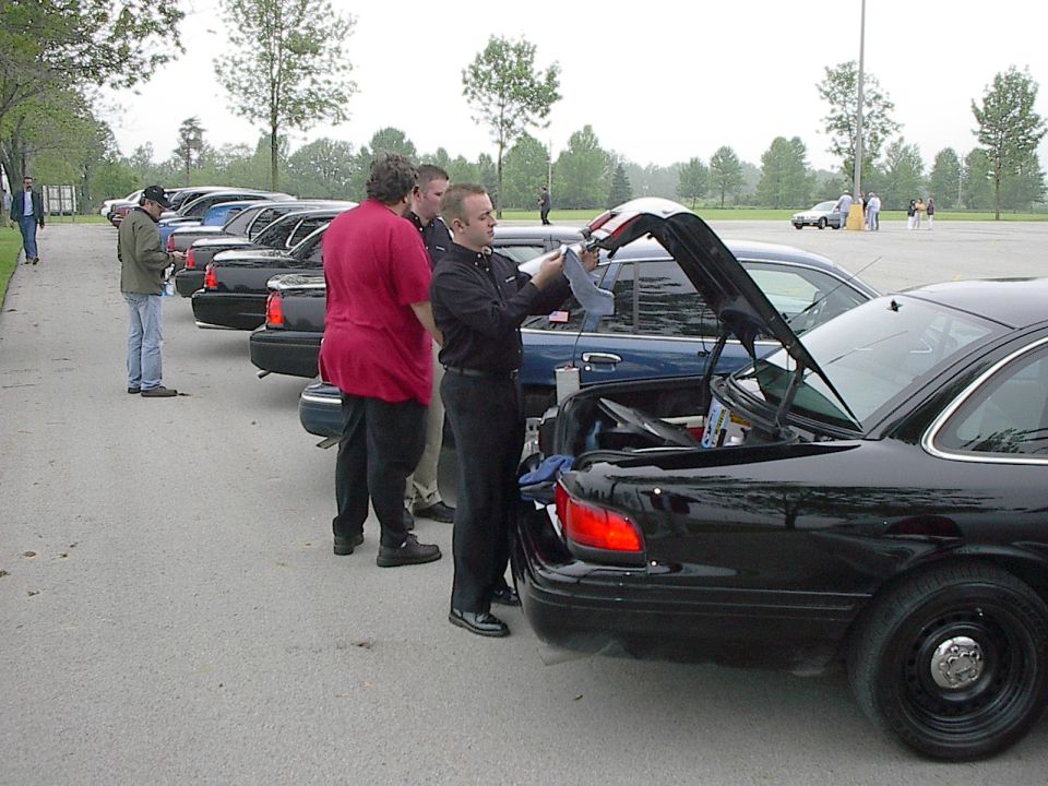 Men gathered around open trunks of black sedans.
