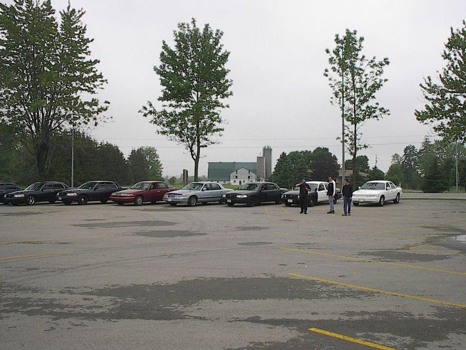 Several sedans parked in a lot, three men standing near a white sedan.