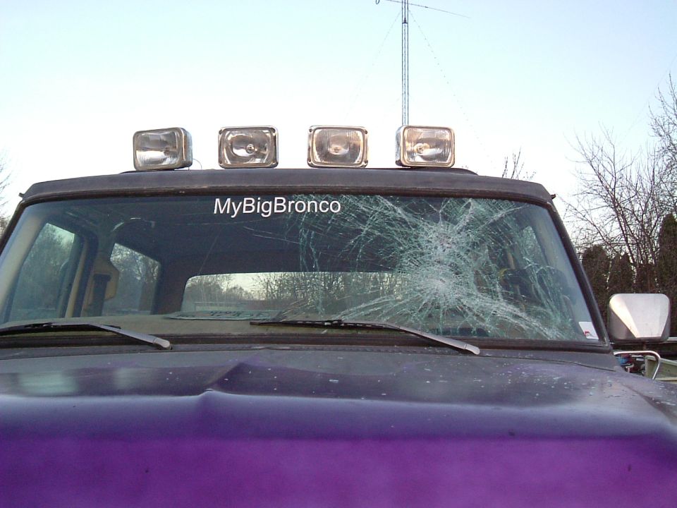 Purple Ford Bronco front view, cracked windshield, four roof lights, "MyBigBronco" sticker on glass