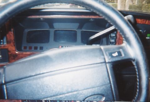 1991 Ford Taurus - The dashboard of a car features wood grain trim and a prominent steering wheel, with a multi-section instrument cluster.