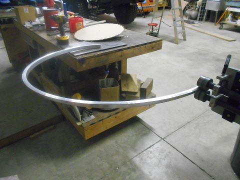 1992 Ford Bronco - A metal bending machine is used to curve a long piece of aluminum. The machine and the aluminum piece are in a workshop setting with tools…