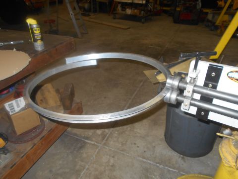 1992 Ford Bronco - A metal ring is being bent into a circle using a metal roller machine. The scene appears to be a workshop with tools and materials in the b…