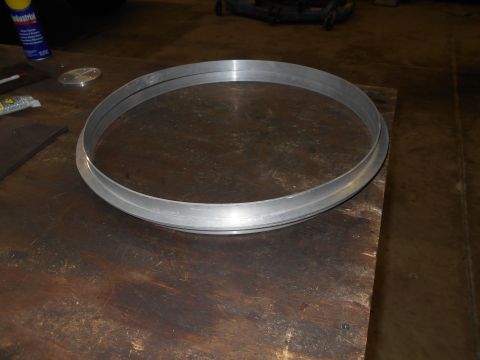 1992 Ford Bronco - A metal ring with two concentric bands sits on a wooden workbench. A can of Industrial lubricant and a small metal disc are visible in the…