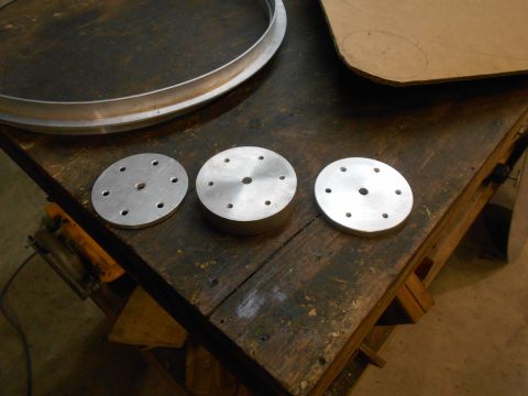 1992 Ford Bronco - Three circular aluminum plates with multiple holes are laid out on a wooden workbench next to a large metal ring and a piece of cardboard w…