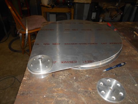 1992 Ford Bronco - A large, irregularly shaped piece of brushed aluminum with red lettering is laid out on a wooden workbench. A small metal disc with six scr…