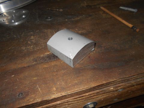 1992 Ford Bronco - A gray, curved metal block with a hole drilled in the center sits on a wooden workbench next to a pencil and a screw.