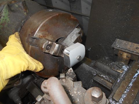 1992 Ford Bronco - A gloved hand is holding a metal part against the jaws of a lathe chuck. Metal shavings are visible on the machine bed.