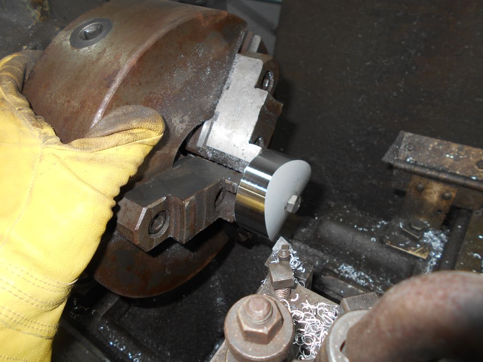 Close-up of a gloved hand holding a metal part against a lathe chuck with metal shavings.