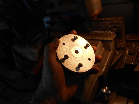 1992 Ford Bronco - A hand holds a circular metal part with several screws protruding from it. The part has concentric circles machined into its surface and a…