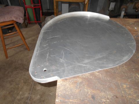 1992 Ford Bronco - A flat, teardrop-shaped piece of brushed aluminum with a beveled edge is resting on a wooden workbench. Several screws and a central hole a…