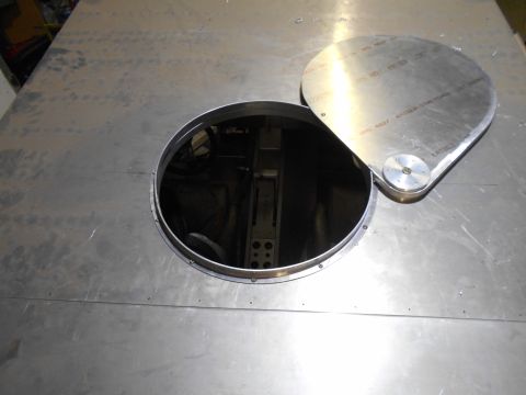 1992 Ford Bronco - A circular access panel has been opened on a flat metal surface, revealing a dark interior. A hinged metal cover with text is propped open…