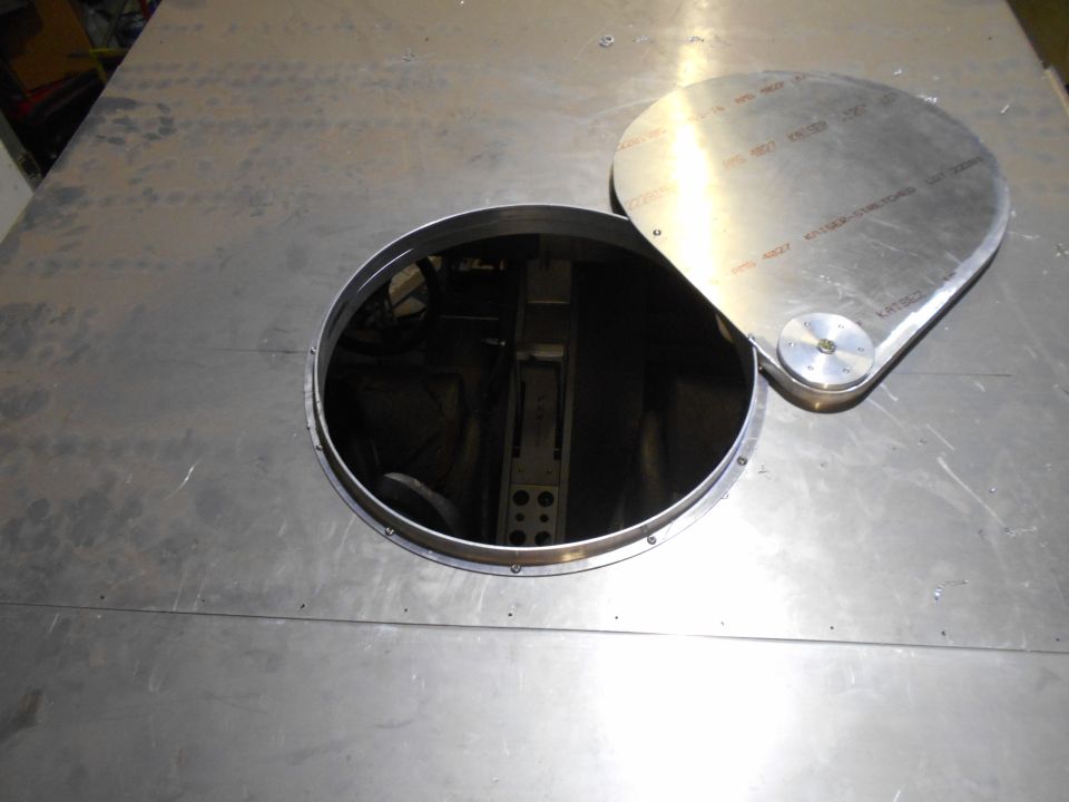 Circular access panel open on a metal surface with hinged cover propped open.
