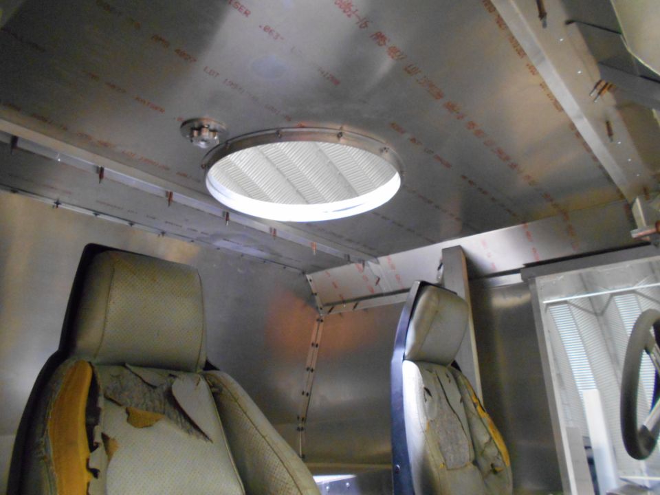 Interior of a vehicle with two worn seats and a metal ceiling with a circular vent.