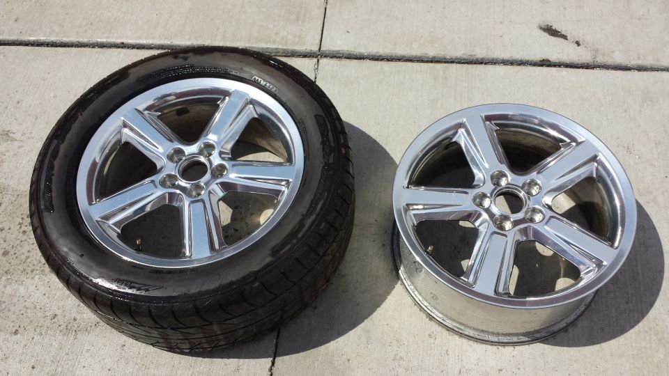 Two chrome five-spoke wheels, one with a tire, on a concrete surface.