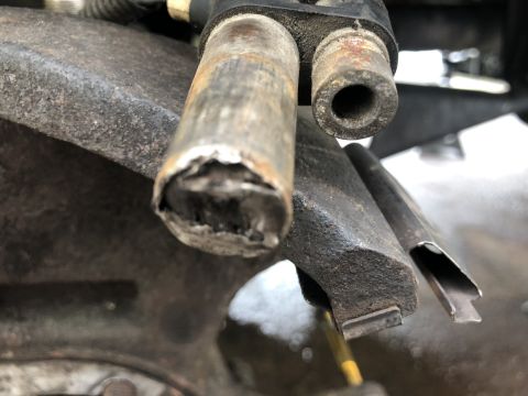 1995 Ford Bronco - A close-up view shows the damaged end of a metal tube, likely a brake line or fuel line, attached to a rusty metal component of a vehicle's…
