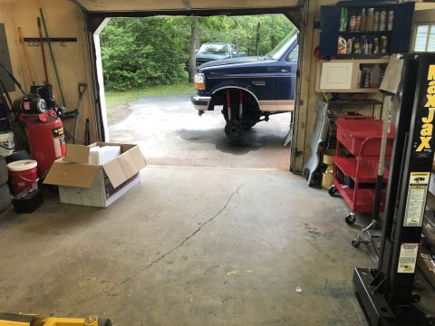 1995 Ford Bronco - A blue Ford Bronco is parked in a garage with its front wheels removed, undergoing maintenance. Various tools and equipment, including an a…