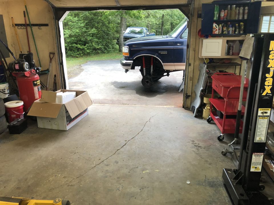 Blue 1995 Ford Bronco in garage with front wheels off, undergoing repairs.