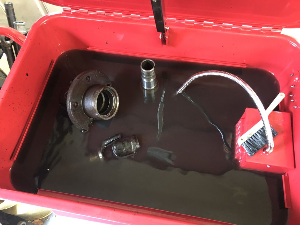 Automotive parts soaking in a red parts washer tub.