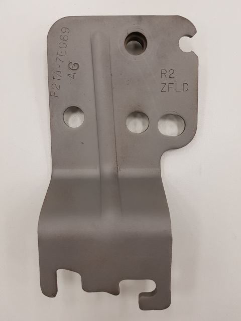 1978 Ford Bronco - A gray metal bracket with stamped text "F2TA-7E069 -AG" and "R2 ZFLD" is shown against a white background. The part has several holes and a…