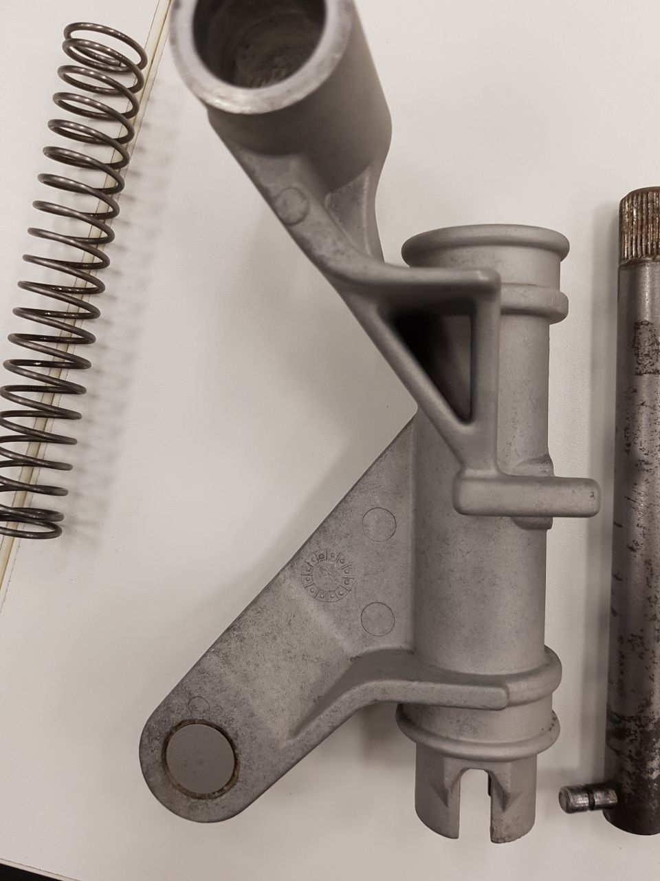 Metal automotive parts including a spring, bracket, and shaft on a white surface.