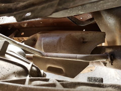 1978 Ford Bronco - Underside view of a vehicle's exhaust system, showing a catalytic converter shield and a metal pipe secured by two bolts.