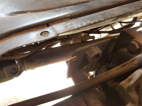 1978 Ford Bronco - A close-up view of the underside of a vehicle, showing a metal bracket with a nut and bolt, a driveshaft, and various hoses and wires attac…
