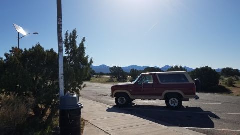 1985 Ford Bronco - A red 1985 Ford Bronco is parked on asphalt under a clear blue sky with mountains in the distance.