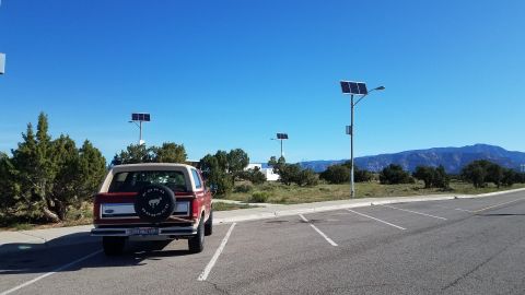 1985 Ford Bronco - A red Ford Bronco with a tan top is parked in a lot under a clear blue sky.