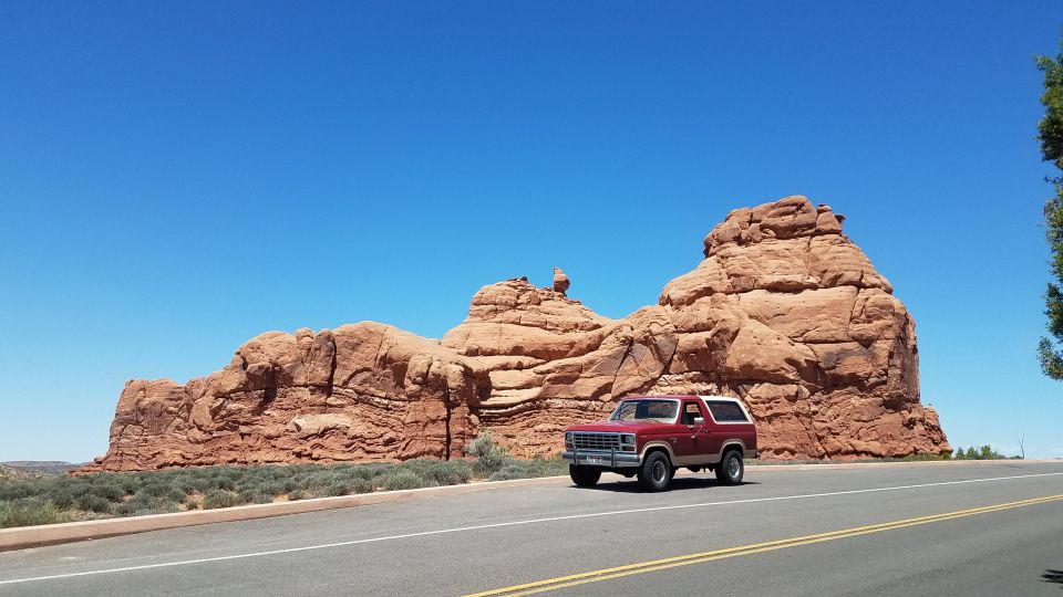 Red Ford Bronco driving on a road with large red rock formations in the background