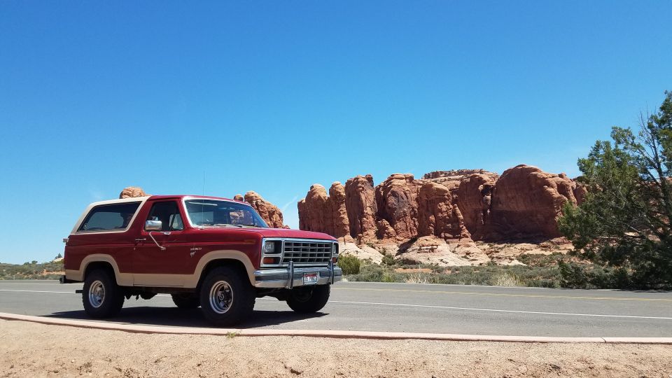 Red and tan 1985 Ford Bronco parked on roadside with red rock formations in background