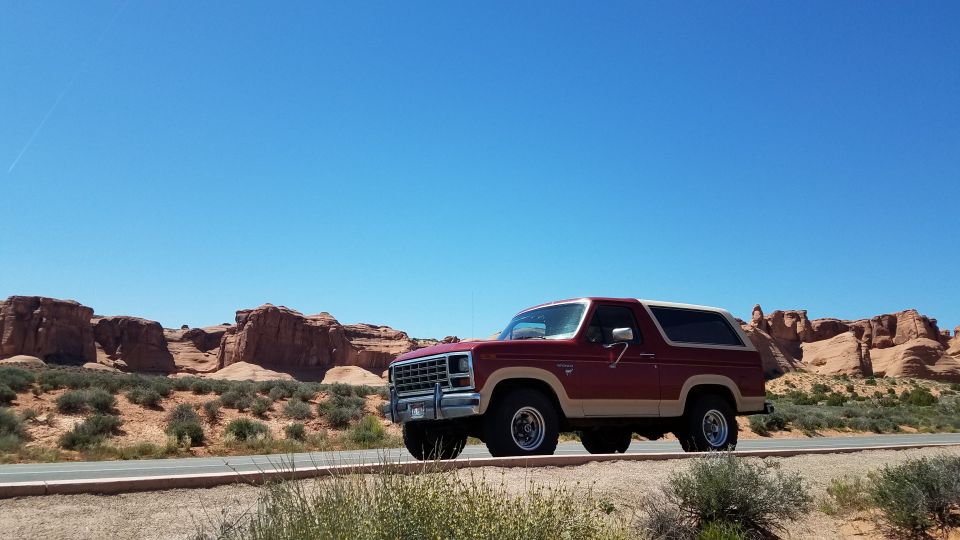 1985 Ford Bronco driving on a road with red rock formations in the background