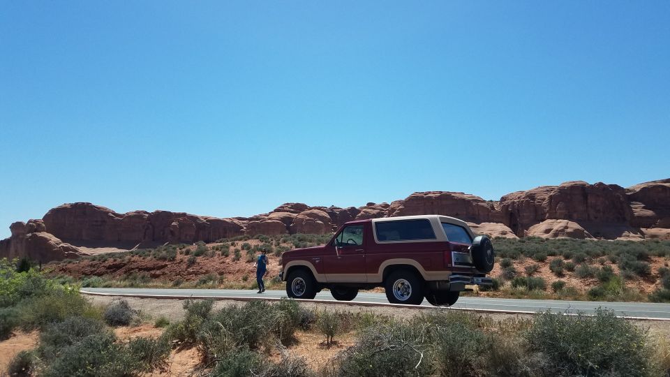 Maroon and tan Ford Bronco parked on a road with red rock formations in the background