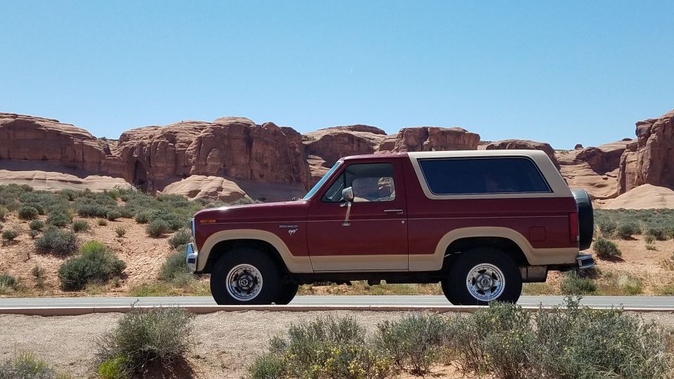 Red and tan Ford Bronco driving on a road with red rock formations in the background