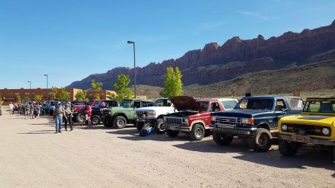 1985 Ford Bronco - A group of Ford Broncos are parked in a lot with a mountainous backdrop under a clear blue sky.