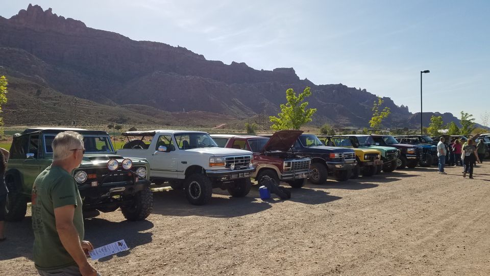 Line of Ford Broncos and trucks, one green, one white, one red with hood up