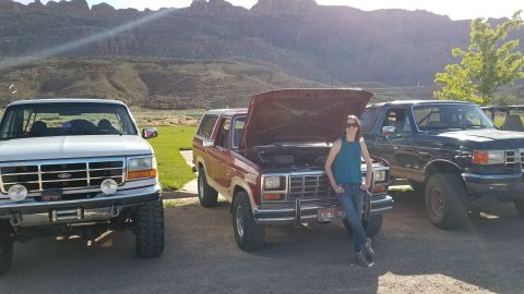 1985 Ford Bronco - Three Ford Broncos are parked outdoors with a woman leaning against the middle one.