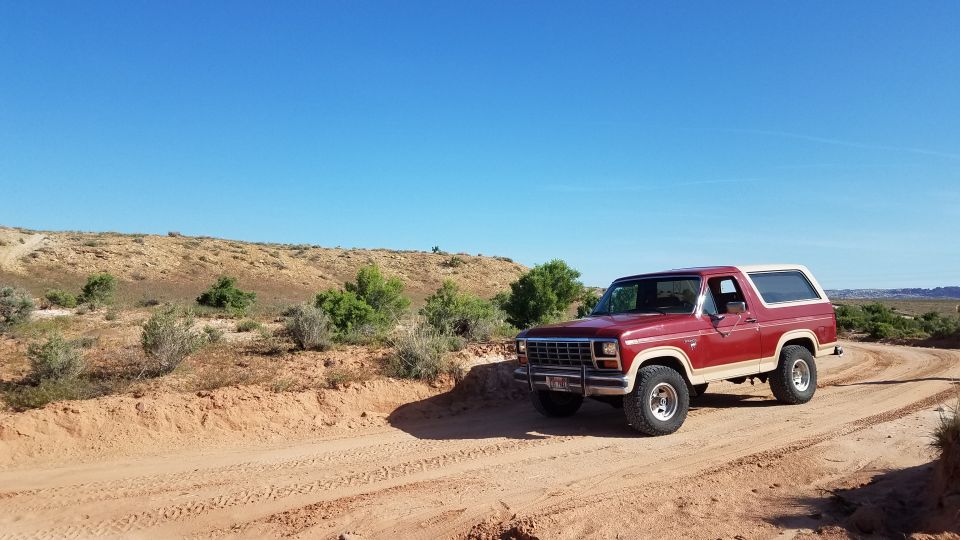 Red 1985 Ford Bronco with white top on dirt road