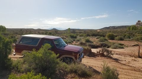 1985 Ford Bronco - SUV parked on a dirt road in a desert landscape with hills in the background.