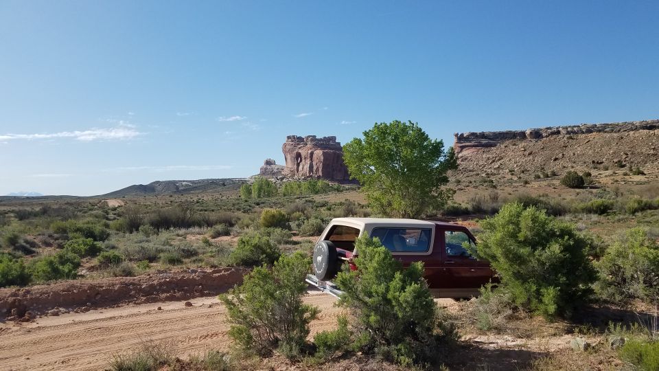 Red Ford Bronco parked on dirt road with rock formations and trees in background